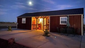 Una construcción de madera con un porche y un vestíbulo cubierto, un pequeño jardín con un calabaza, y un patio con mobiliario exterior.