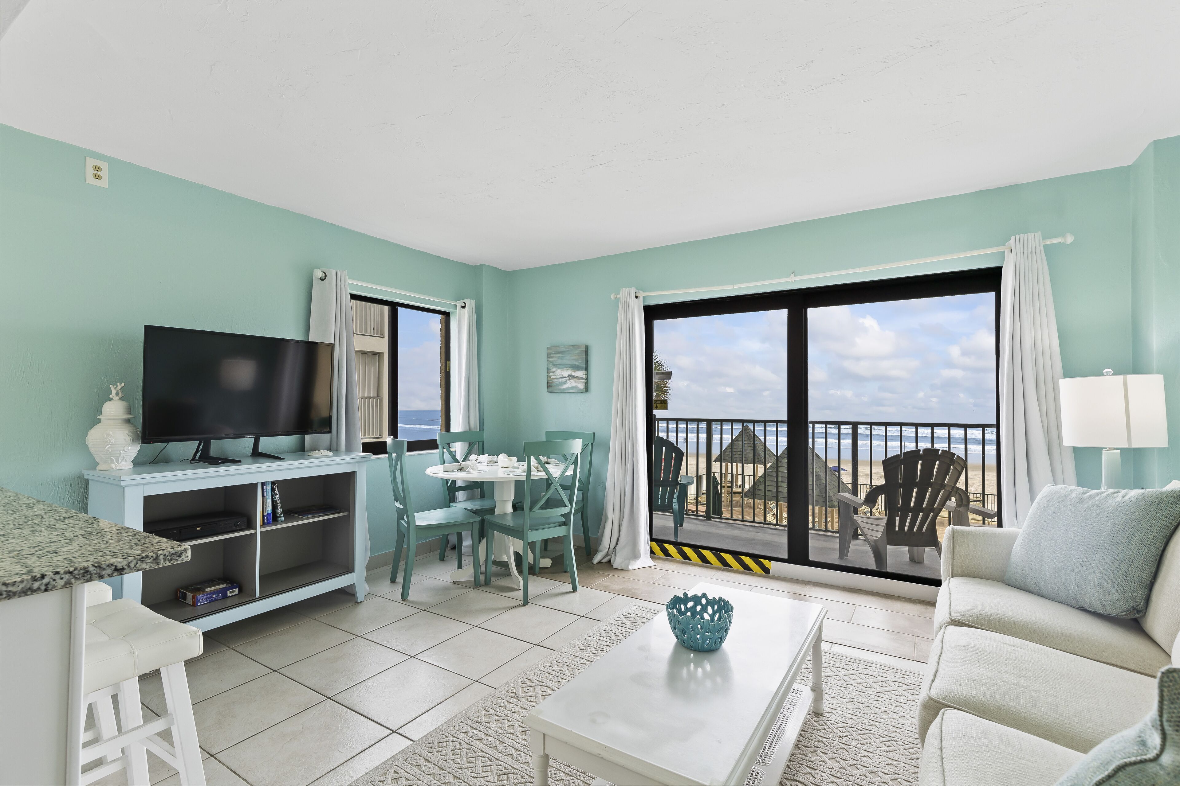 Un salon comprenant un téléviseur, une table à manger, des chaises et un canapé. Il y a également un balcon avec vue sur la plage.