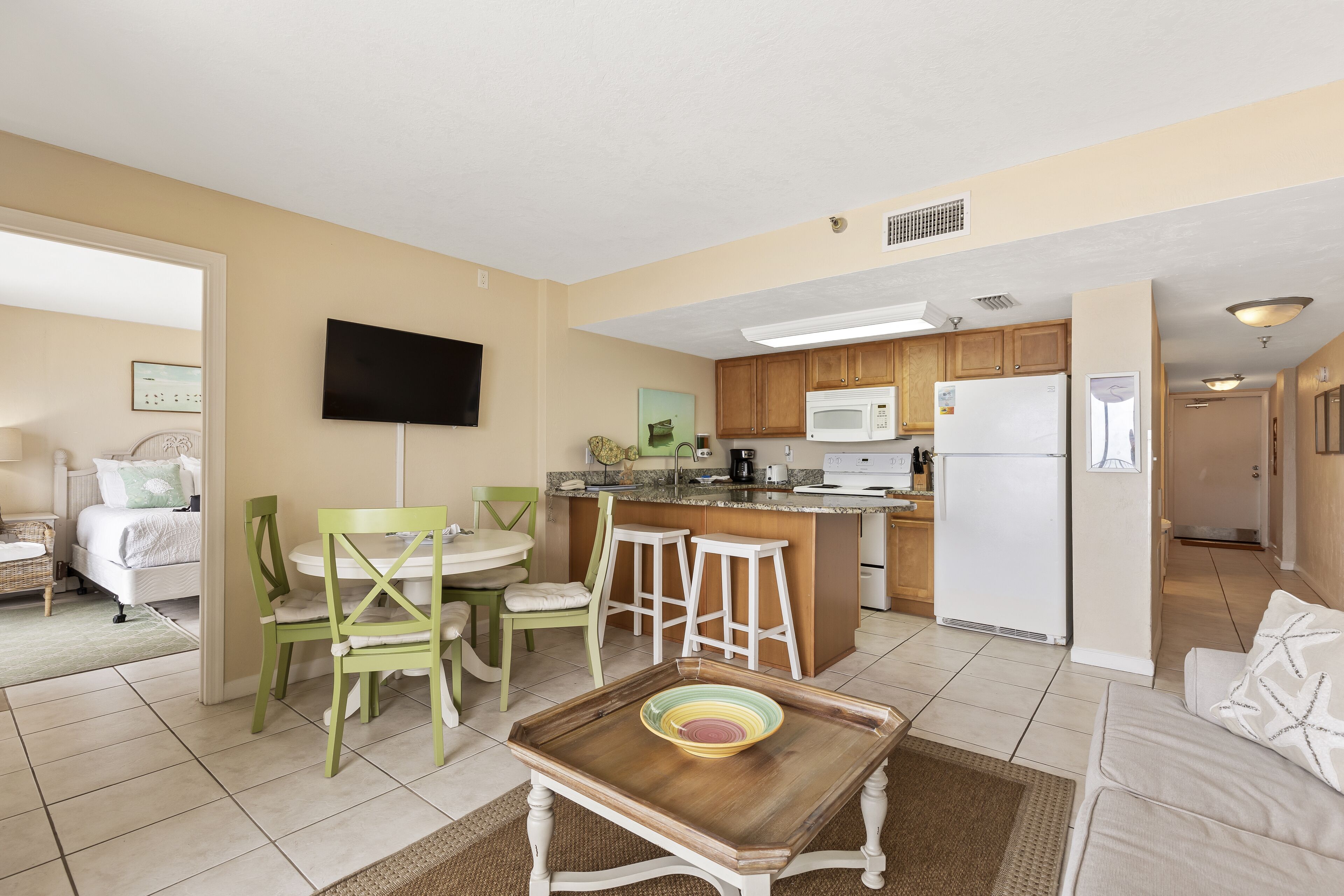 A compact living space with a kitchenette, a dining area with a table and chairs, a sofa, and a TV mounted on the wall.