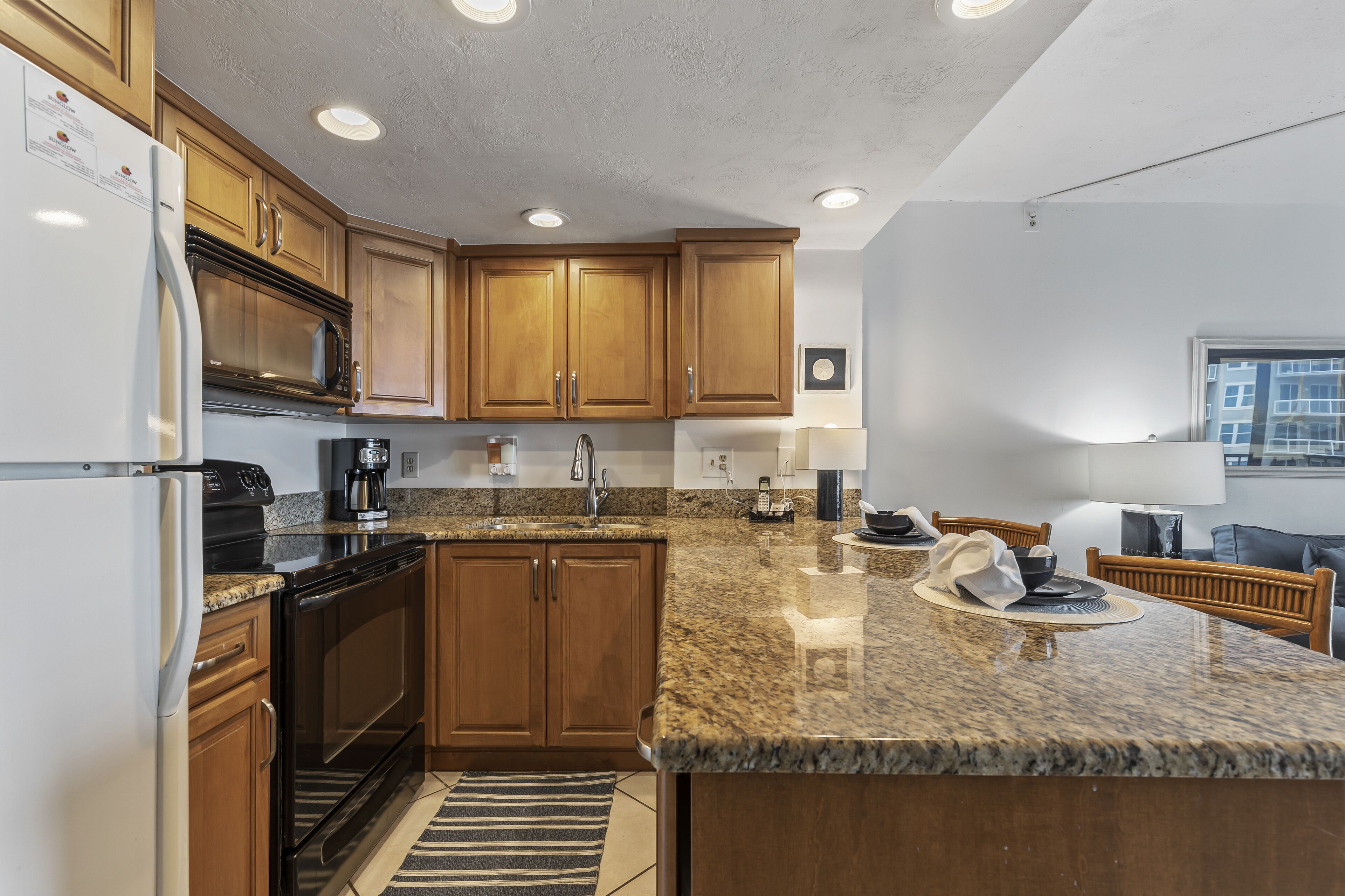 A modern kitchen with granite countertops, wooden cabinets, a built-in oven, and a stainless steel range hood.
