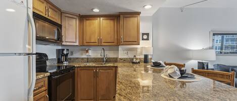 A modern kitchen with granite countertops, wooden cabinets, a built-in oven, and a stainless steel range hood.
