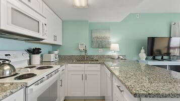 A modern kitchen with white cabinets, a granite countertop, a microwave, stove, and a sink.