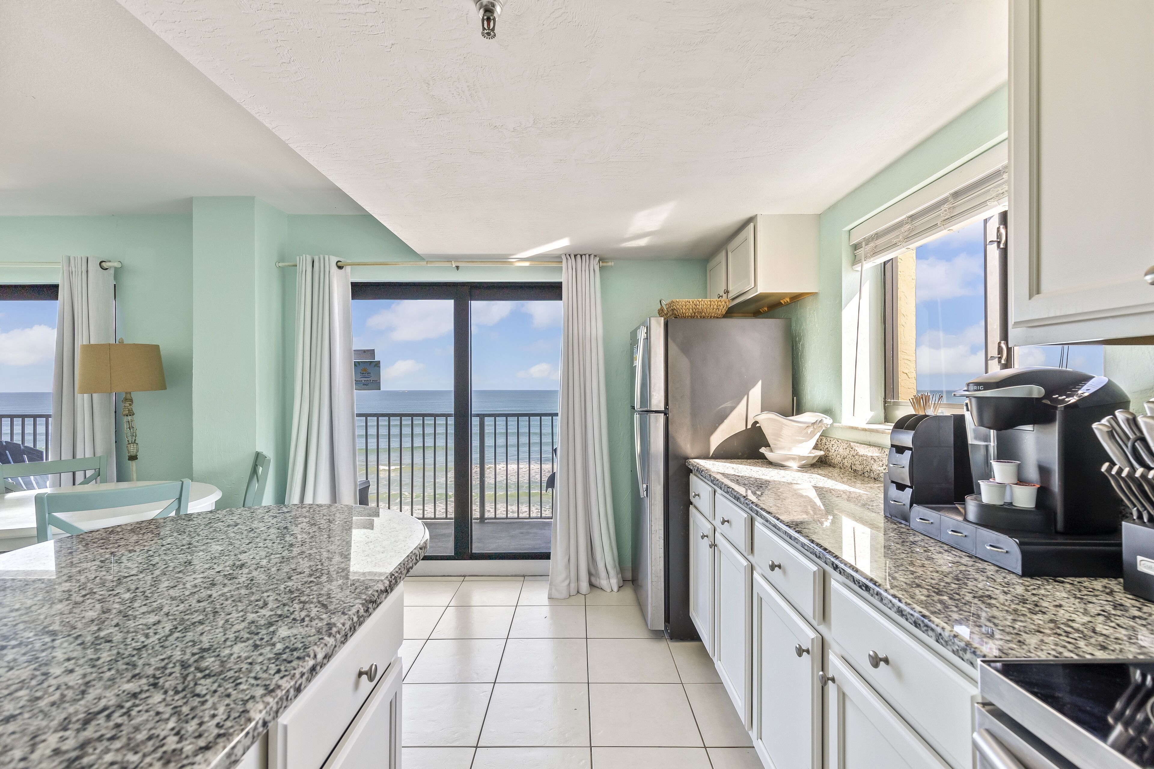A kitchen with a view of the ocean, a dining area with a table and chairs, and a coffee machine.