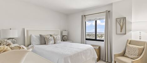 A hotel room with a bed, a chair, a desk, and a window with a view.
