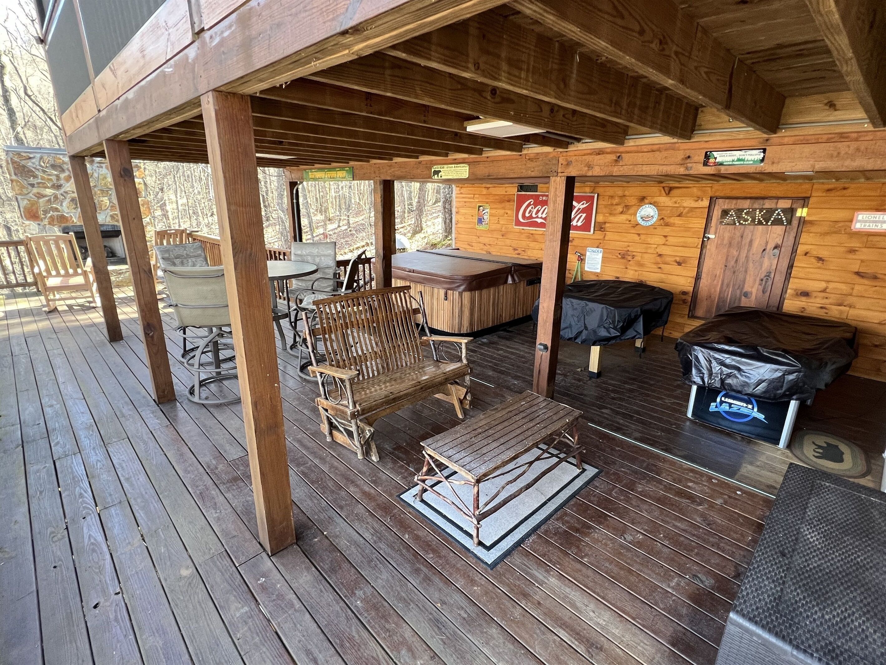 A wooden deck with outdoor seating, a hot tub, and a covered area with signs for Coca-Cola and Aska.