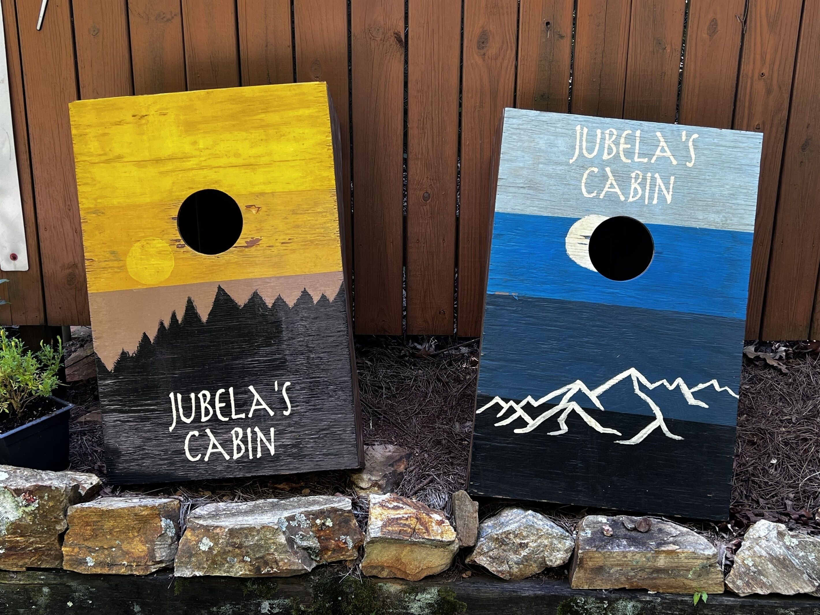 Two wooden signs with cabin names, 'Jubela's Cabin' and 'Jubela's Cabin', placed on a wooden fence.