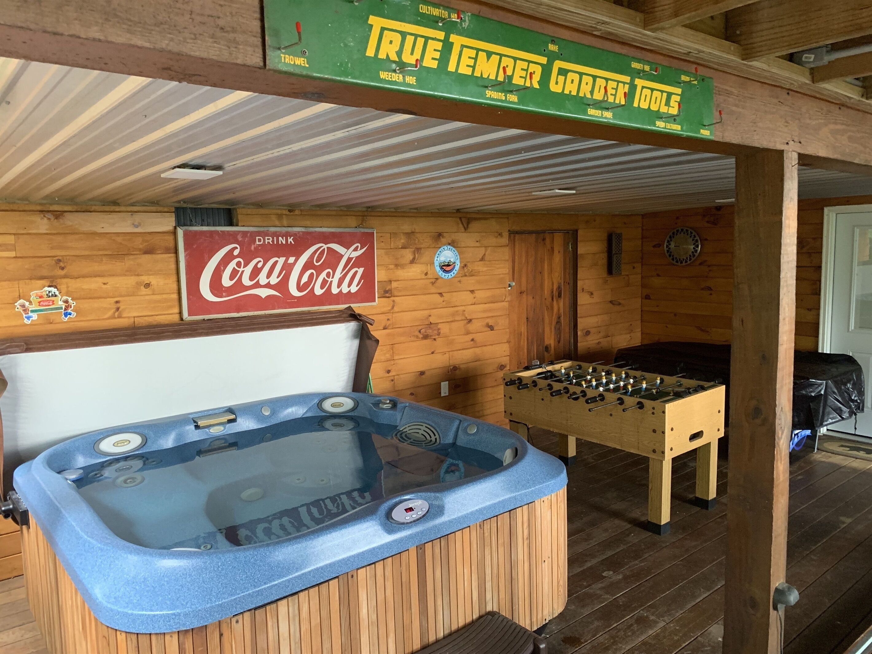 Een houten interieur met een bubbelbad, een tafelvoetbaltafel en een Coca-Cola bord.
