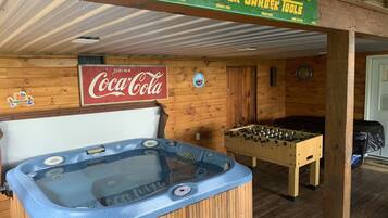 Een houten interieur met een bubbelbad, een tafelvoetbaltafel en een Coca-Cola bord.