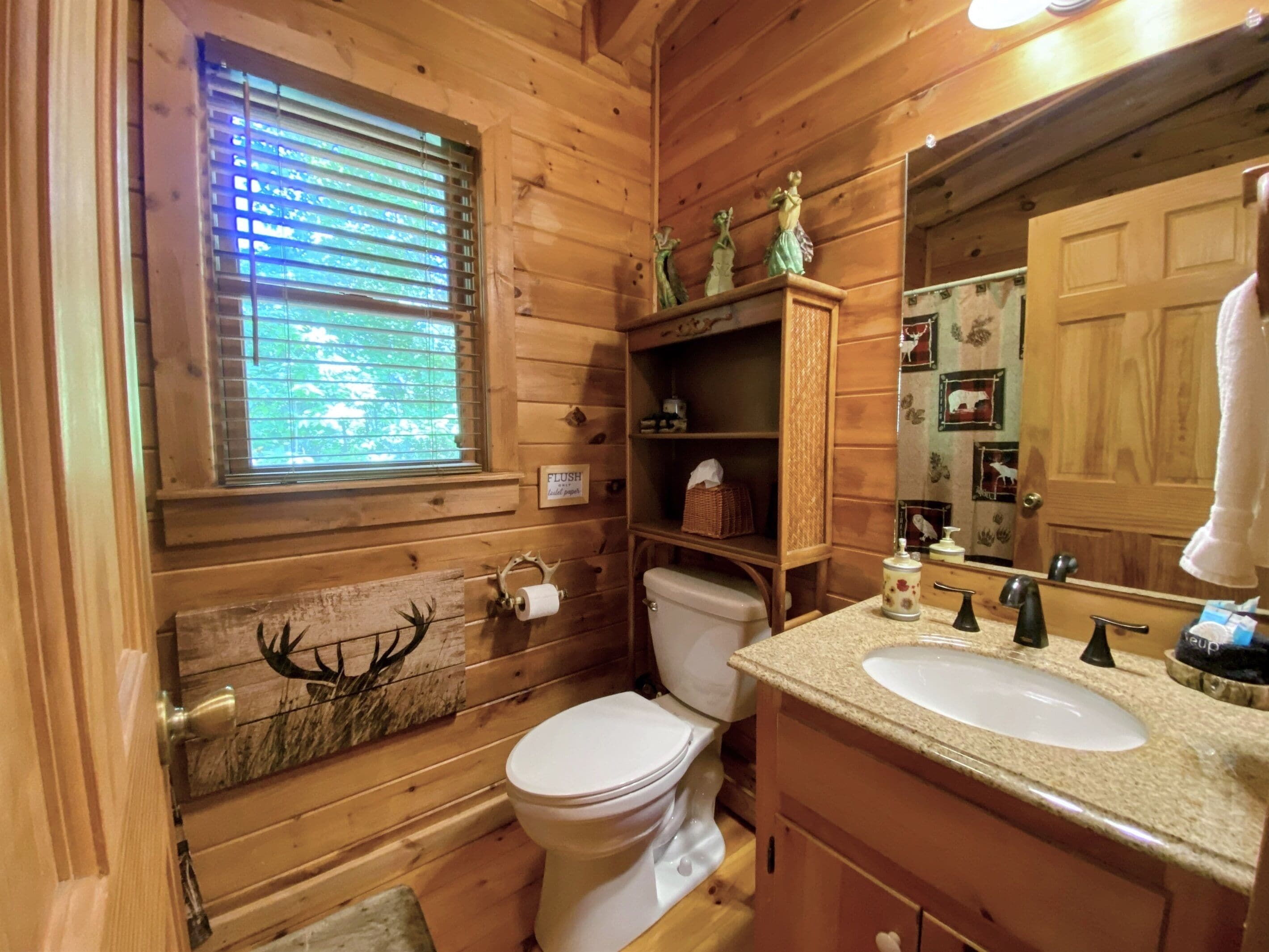 A wooden cabin bathroom with a toilet, sink, and window with blinds.