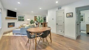 Una sala de estar moderna con chimenea, un comedor con una mesa redonda y sillas, y una cocina al fondo.