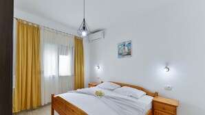 Ein Schlafzimmer mit einem hölzernen Bett, gelben Vorhängen, einer Wand-Klimaanlage und einem Gemälde.