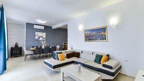 Ein modernes Wohnzimmer mit einer Eckcouch, einem Essbereich mit Tisch und Stühlen und einem großen Stadtbild an der Wand.