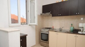 A compact kitchen with a stove, oven, and sink. There is a window with an open door, and cabinets above the counter.