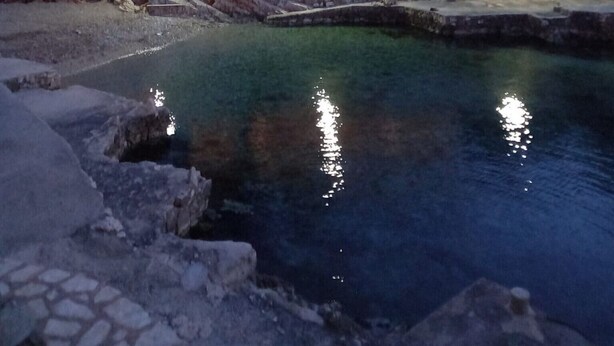 A stone-walled pool with a clear water surface reflecting lights, surrounded by a stone pathway.