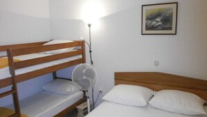 A bunk bed room with a standing fan, a single bed, and a framed picture on the wall.