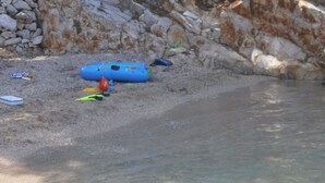 A rocky shoreline with a blue raft and various water sports equipment.