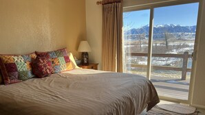 Une chambre avec un grand lit, une table de chevet avec une lampe, et une vue sur un paysage enneigé par une porte coulissante.