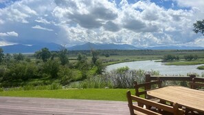 Overlooking a serene river, this outdoor space offers a peaceful retreat with a deck and seating area surrounded by lush greenery and majestic mountains.