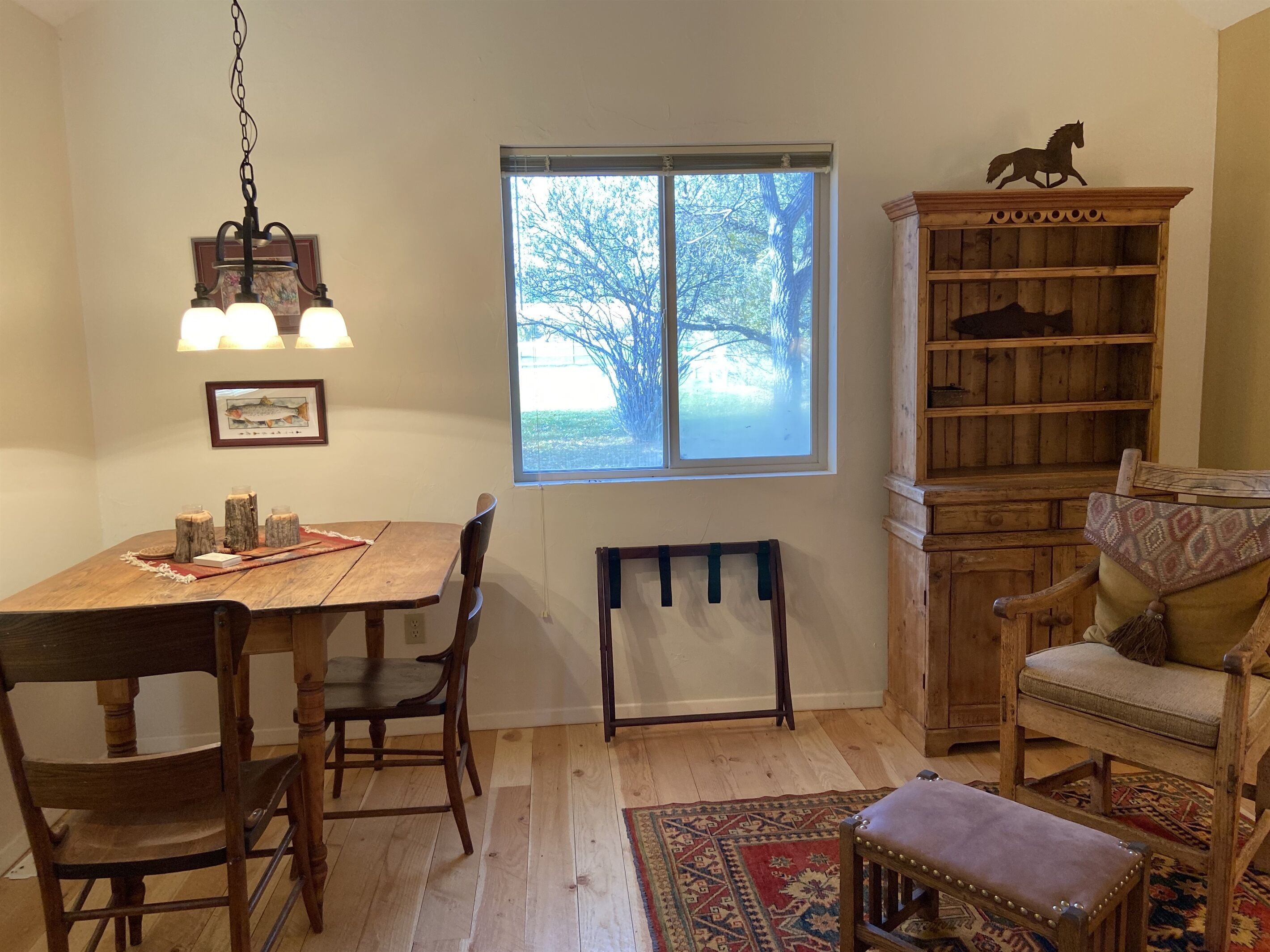 Un coin repas avec une table en bois, des chaises, un luminaire suspendu, une fenêtre donnant sur des arbres et une bibliothèque.