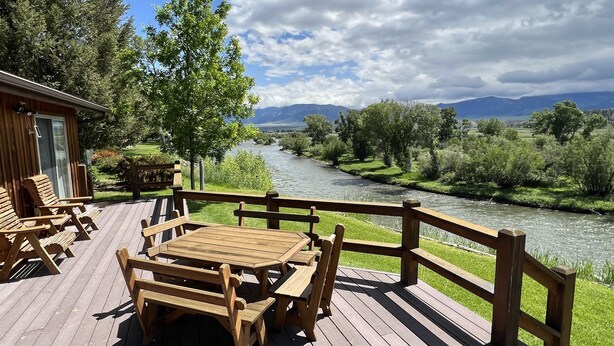Une terrasse en bois, agréée de mobilier d’extérieur, qui offre une vue sur une rivière et des montagnes.