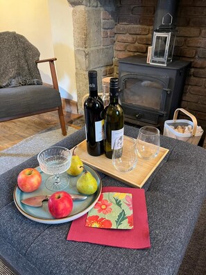 Ein gemütliches Wohnzimmer mit Kamin, einem Esstisch mit Weinflaschen, Gläsern und Obst.
