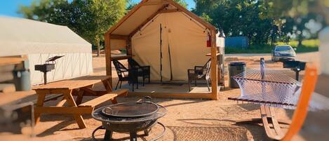 A camping site with a tent, picnic table, chairs, and a fire pit.