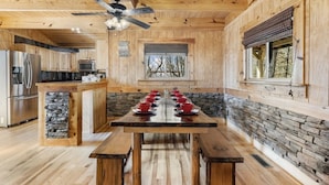 Une cuisine rustique dans une cabane en bois, avec un mur d’accent en pierre, un îlot central orné de tasses rouges et un ventilateur de plafond.