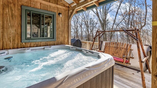 Un bain à remous installé sur une terrasse en bois, avec vue sur les arbres et un portique.