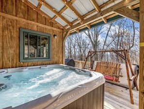 Un bain à remous installé sur une terrasse en bois, avec vue sur les arbres et un portique.