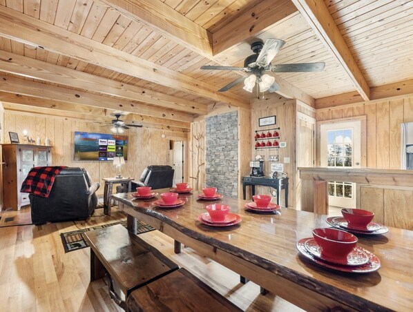 Un intérieur en bois avec une longue table à manger, dressée avec des tasses et des soucoupes rouges, un fauteuil en cuir noir et un mur en pierre.