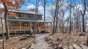 Un chalet rustique avec une façade en bois, une véranda et un chemin de pierre menant à l’entrée.