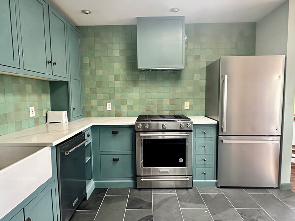 A kitchen with teal cabinetry, a stainless steel refrigerator, a double oven, and a white countertop.