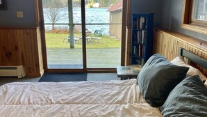 Ein Schlafzimmer mit einem großen Bett, einem hölzernen Kopfteil, einem Bücherregal und Seeblick durch eine Schiebetür.