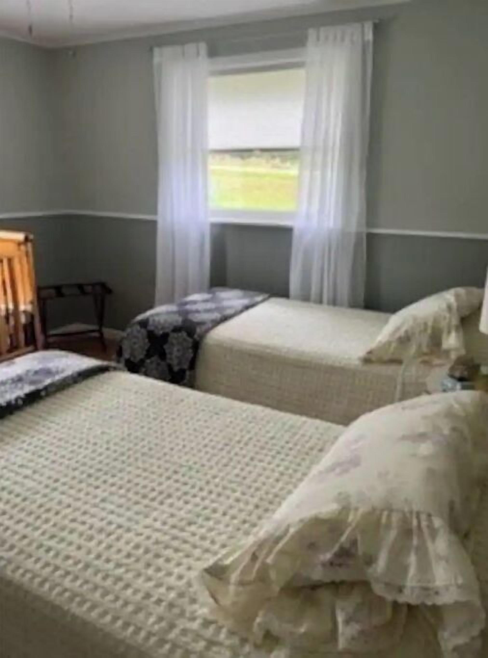 A room with two beds, a chair, and a window with curtains.