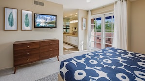 Un dormitorio con cama, cómoda, televisor y vistas a un baño y zona exterior.