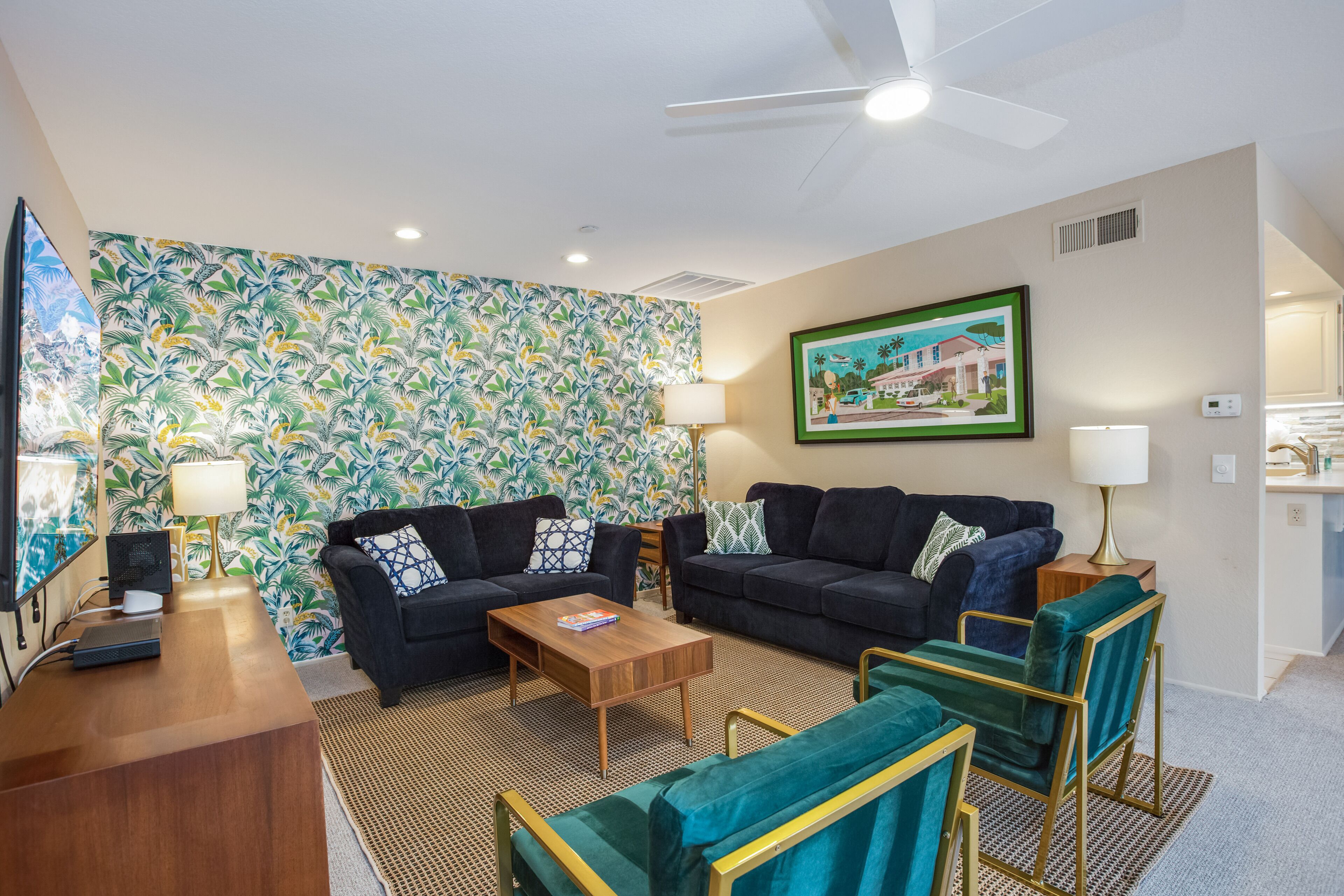 A modern living room with a tropical wallpaper, two dark sofas, a wooden coffee table, and a ceiling fan.