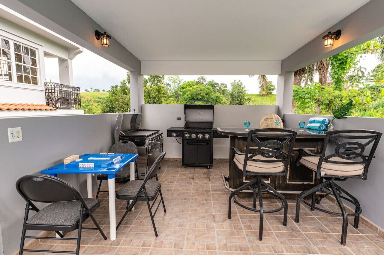 Terrassa a l'aire lliure amb una barbacoa, taula de menjador, cadires i una taula blava amb objectes a sobre.