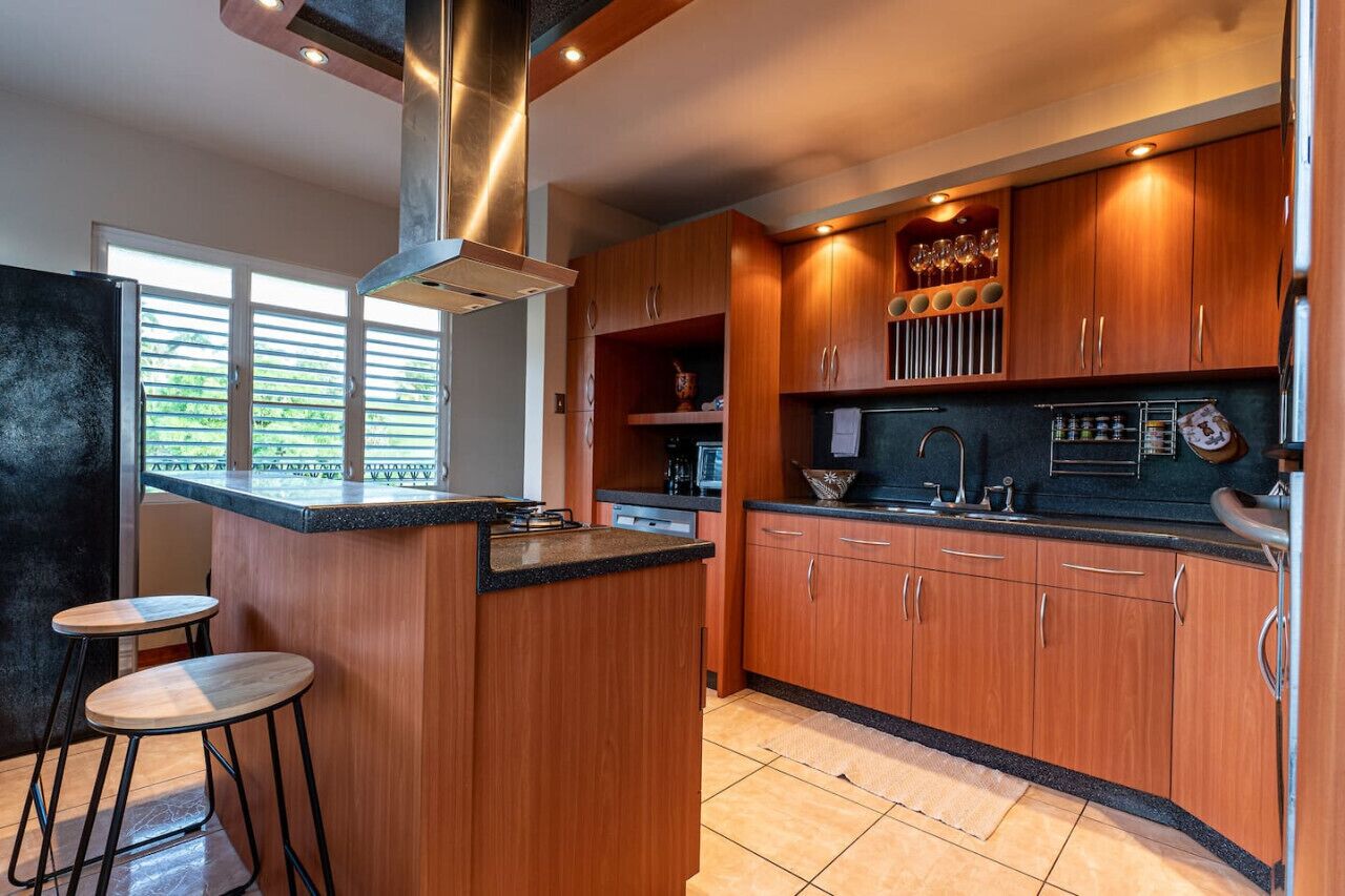 A modern kitchen with wooden cabinets, a central island with stools, and a stainless steel range hood.