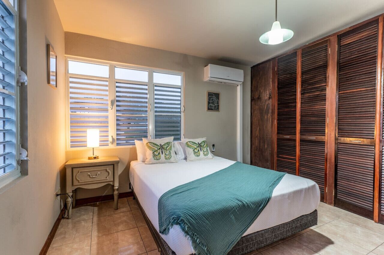 A bedroom with a bed, bedside table, lamp, window with shutters, and a wardrobe.