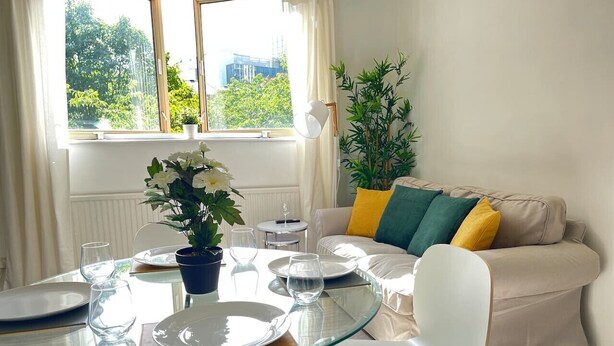 A dining area with a glass table, white chairs, and a sofa with colorful cushions. - London Central 2 Bathroom Flat with Free Parking (London)