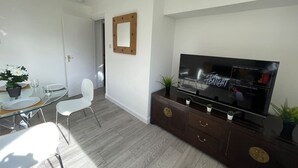 A modern living room with a flat-screen TV, a dining area with a glass table and chairs, and a hallway leading to another room. - London Central 2 Bathroom Flat with Free Parking (London)