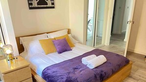 A bedroom with a wooden bed, white bedding, a purple throw blanket, and a nightstand with a lamp. - London Central 2 Bathroom Flat with Free Parking (London)