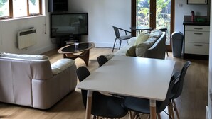 A modern living room with a sofa, dining table, and chairs, a television, and a window with blinds.
