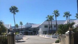 A gated entrance to a hotel with a clear sky, palm trees, and a building with a sign that reads "The Salt Mill."