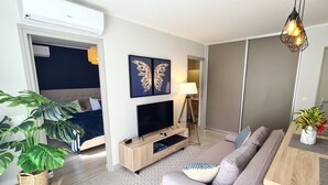 A modern living room with a sofa, TV, and a large plant. - Appart Hitivai by Tahiti Homes (Papeete)