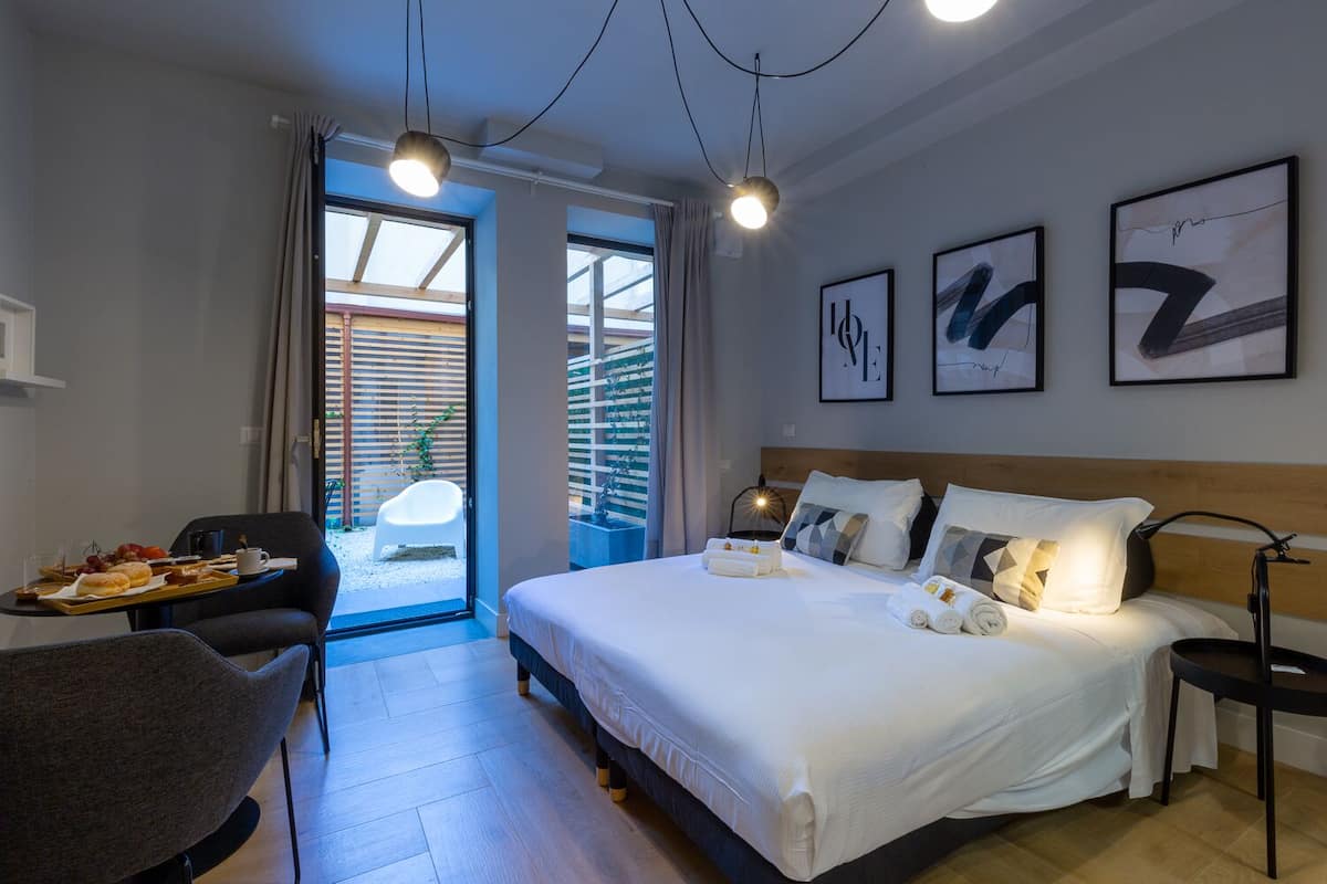 A hotel room with a bed, bedside table, and a view of the outside.