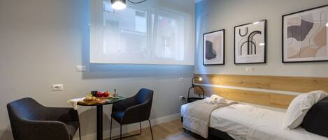 Una habitación de hotel moderna con una cama, una pequeña mesa de comedor con sillas, una pantalla de proyector y obras de arte en las paredes.