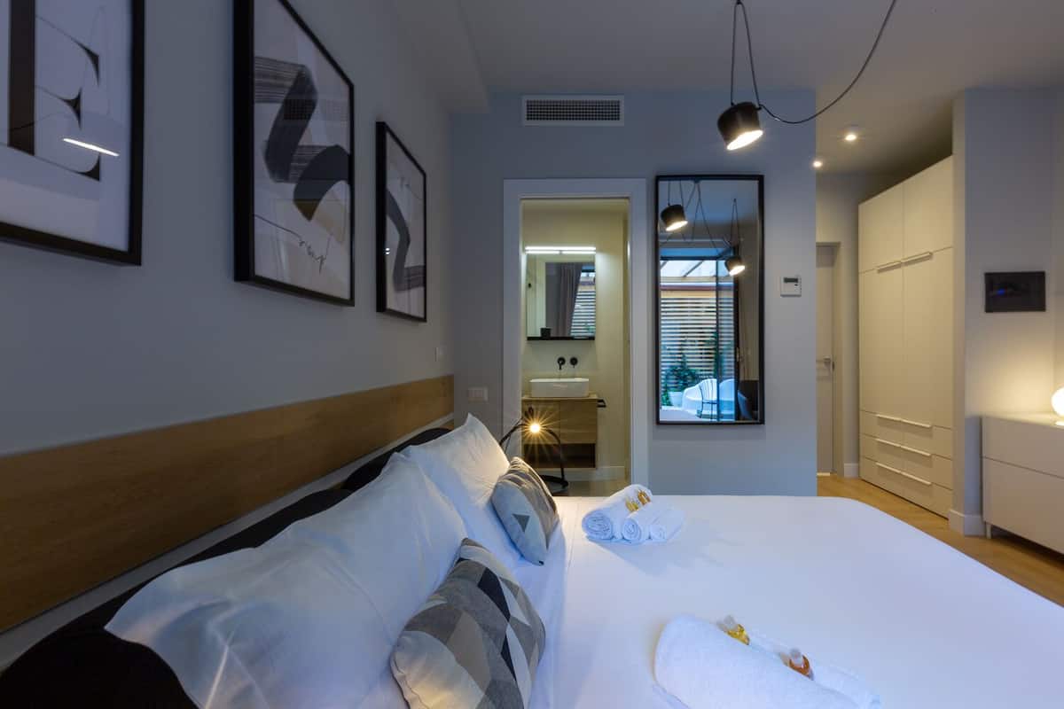 A modern hotel room with a large bed, a bathroom with a sink, and a view of the outside through a window.