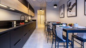 A modern kitchen with black cabinets, a black countertop, and a dining area with blue chairs and a table set for two. - Casa Lounge 43 (Cagliari)