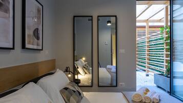 A modern hotel room with a large bed, two mirrors, and a view of a wooden deck and greenery outside.